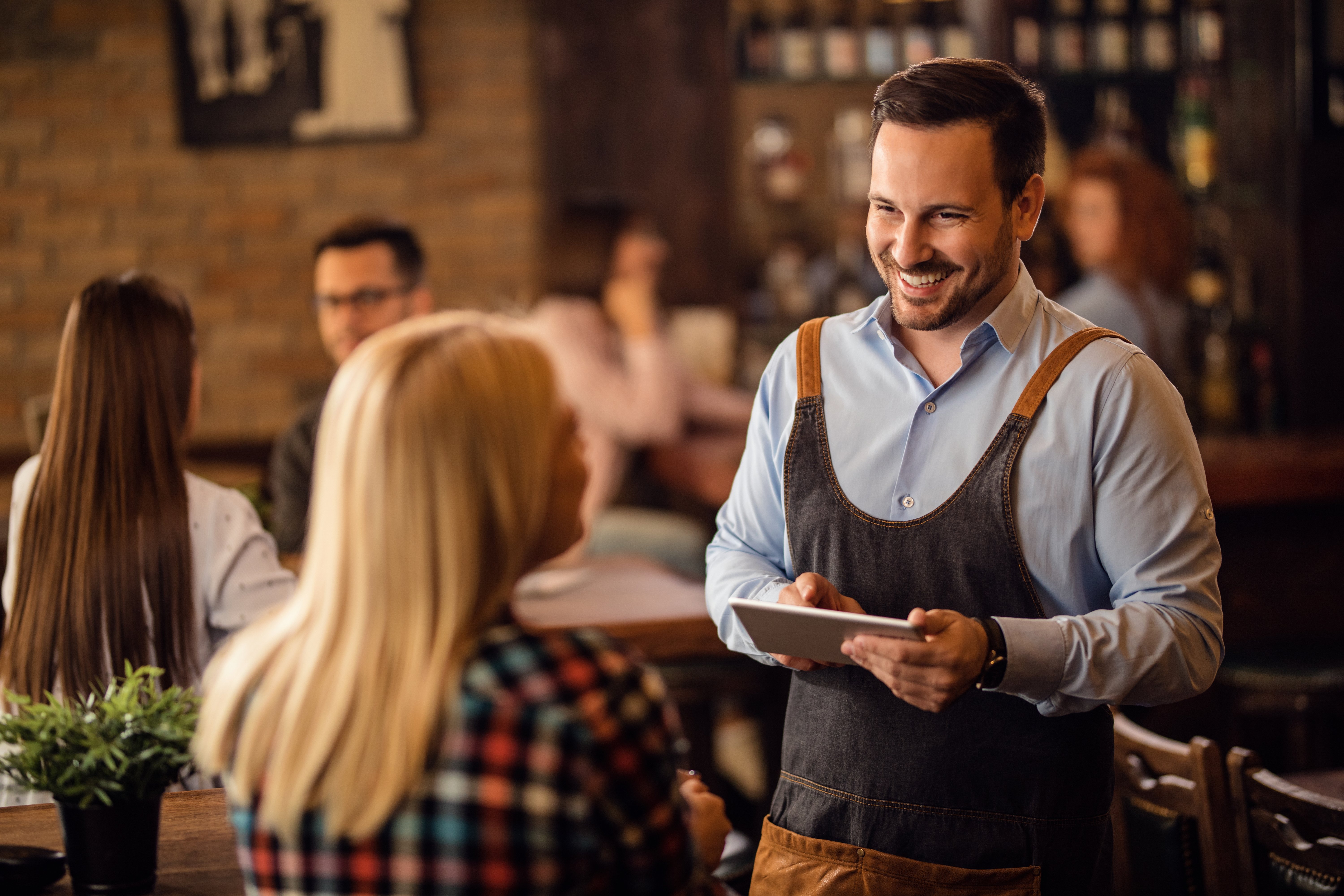 happy-waiter-talking-female-customer-writing-her-order-digital-tablet-bar
